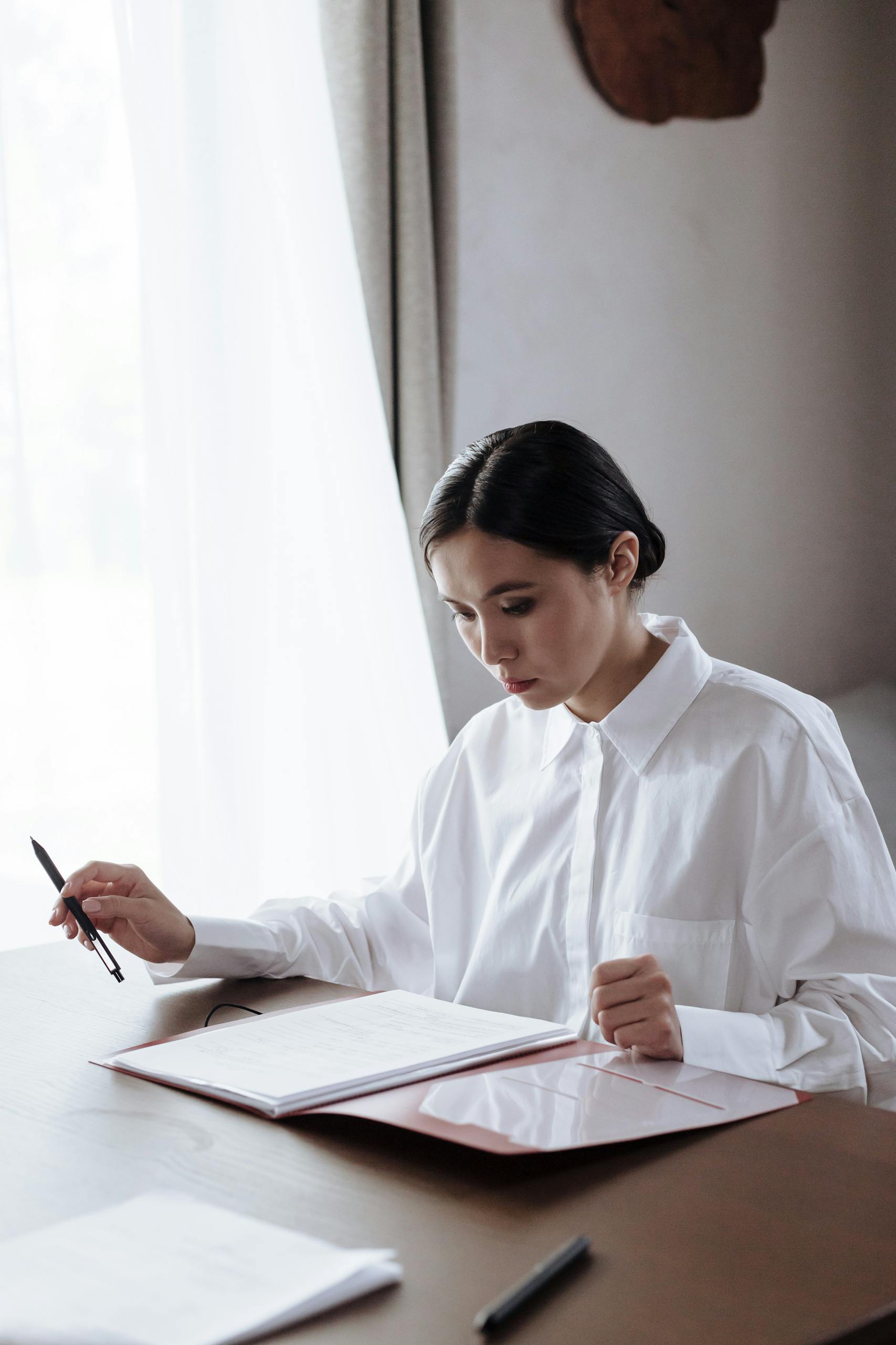 A woman in a white shirt diligently reviewing documents at a home office desk.