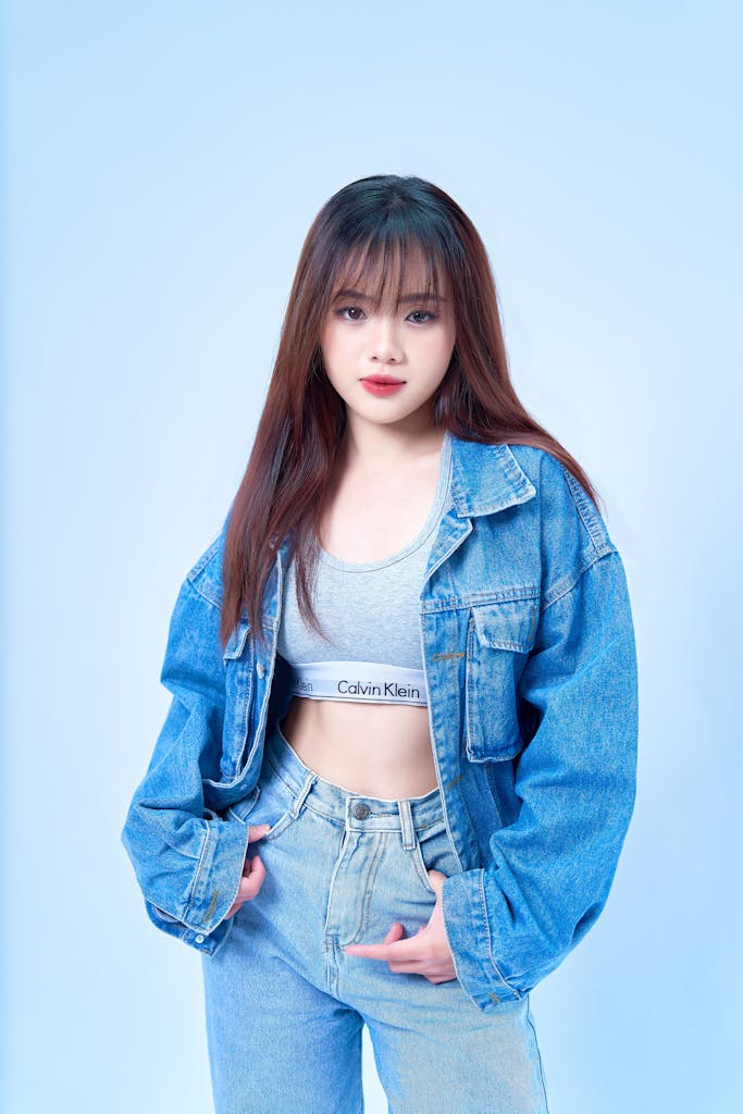 Fashionable woman in denim jacket and jeans posing in studio, showcasing casual style.