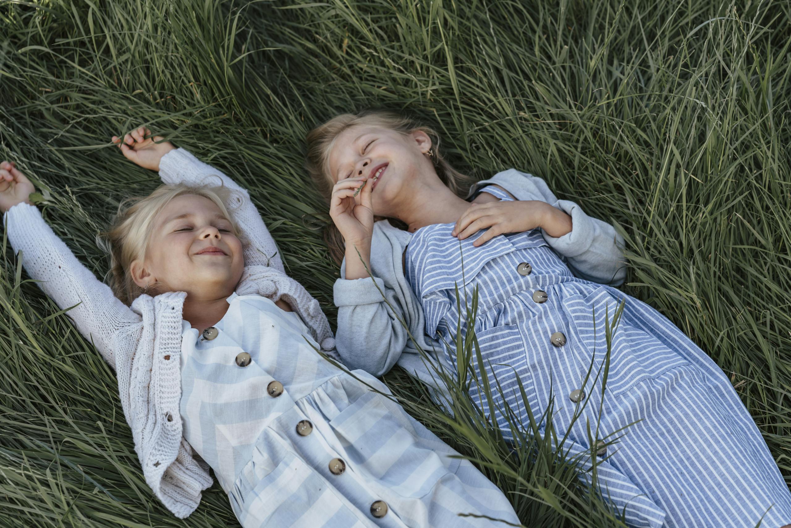 Two young girls happily lying on grass, enjoying a playful moment together.