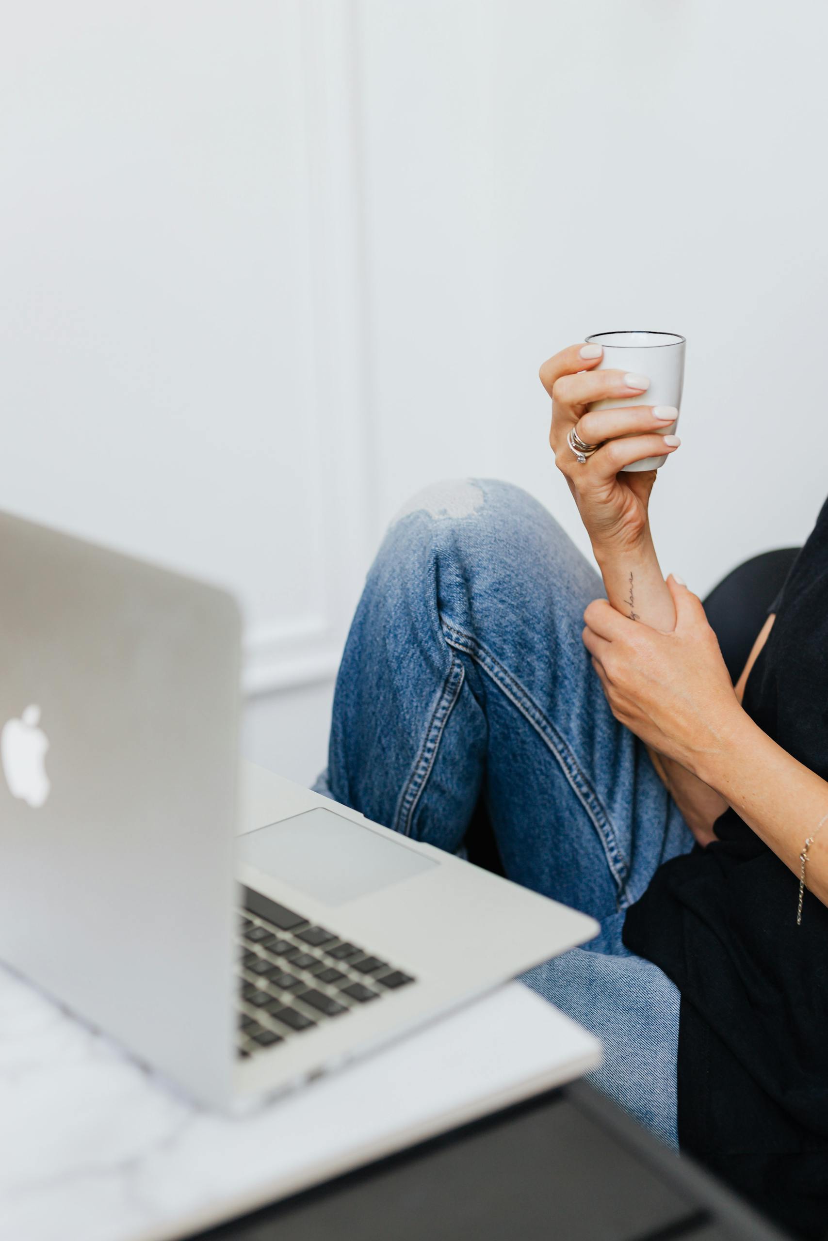 Woman sitting with denim jeans and holding a white mug while using a laptop